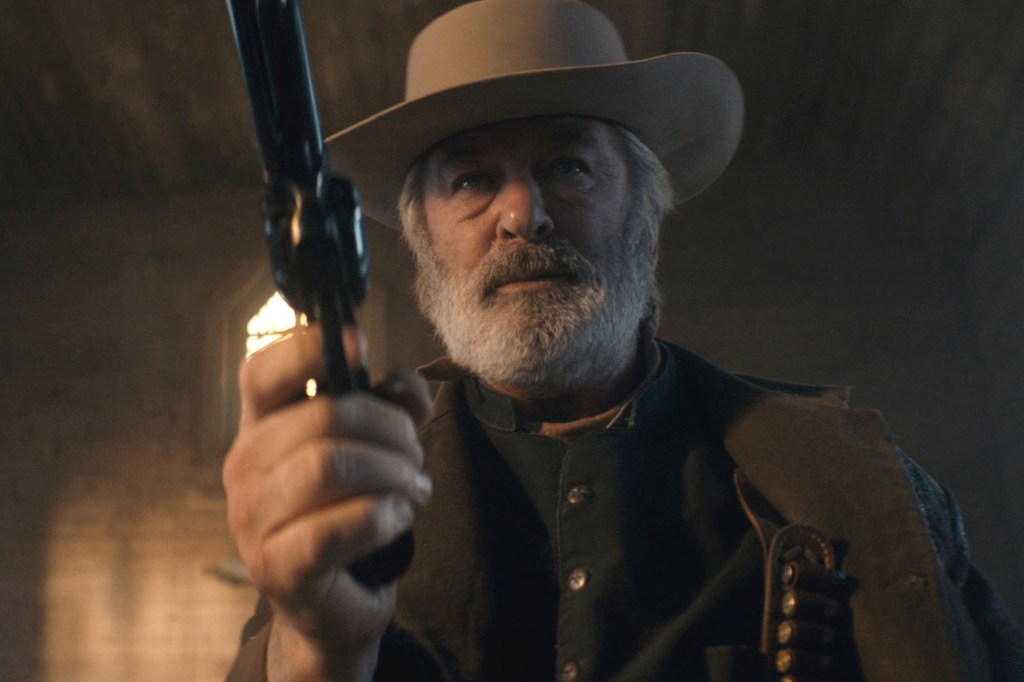 Alec Baldwin as Rust, holding a prop gun in a low-angle shot.