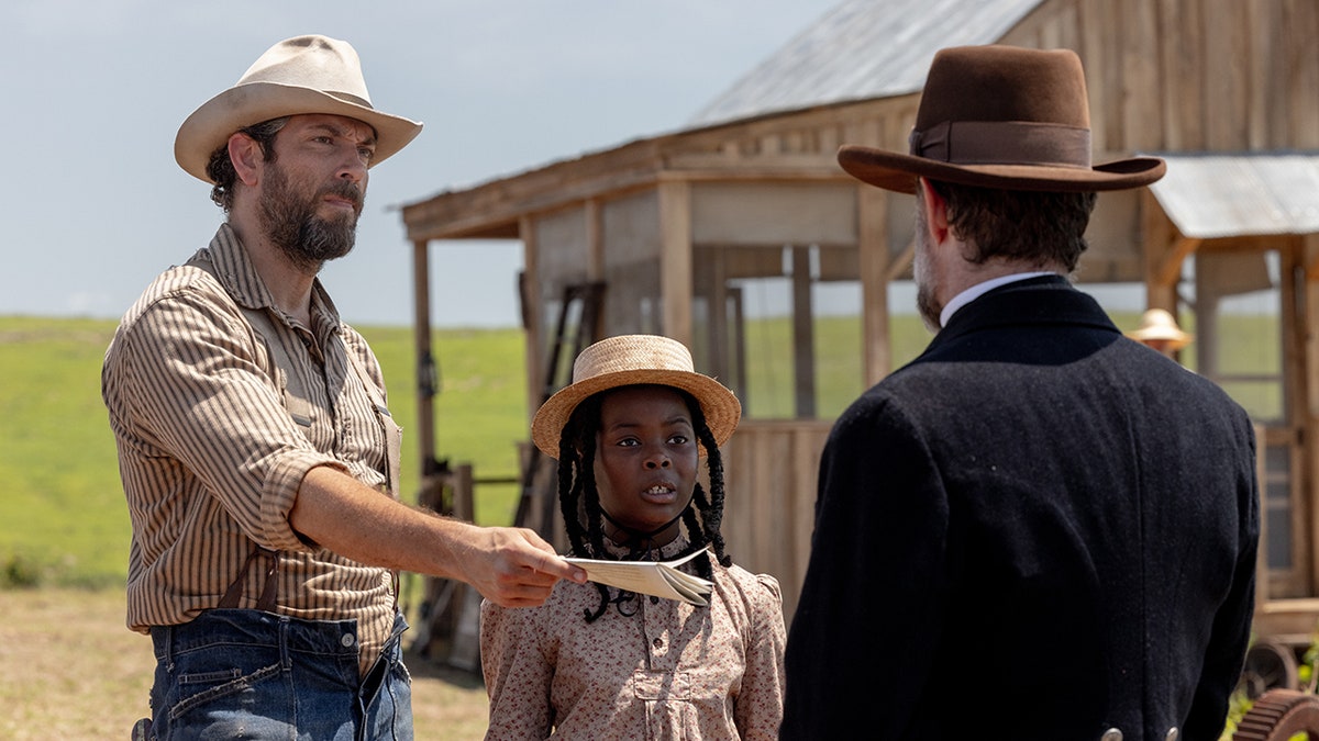 Zachary Levi holds out a document while standing beside his co-star in the film "Sarah's Oil."