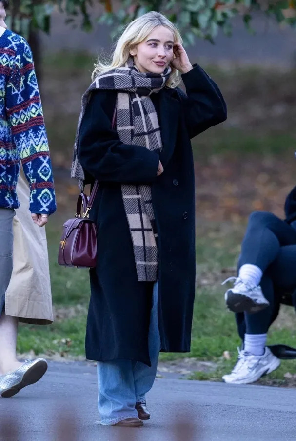 Sabrina Carpenter wrapped in a plaid scarf and black coat while walking outdoors