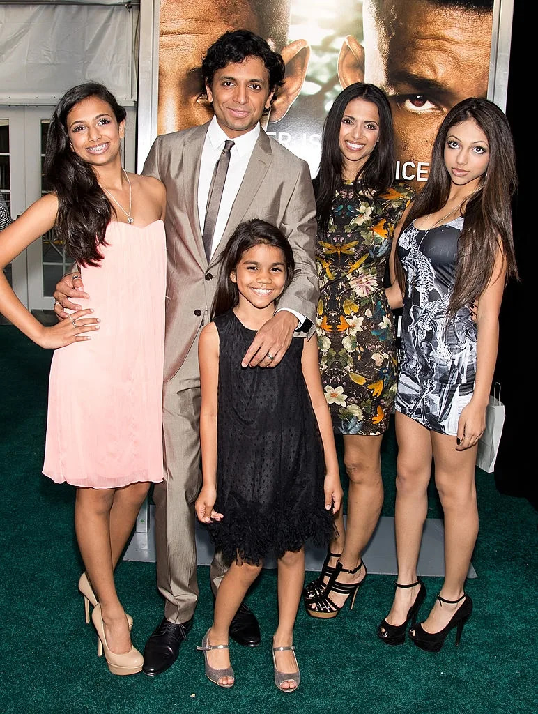 Five people posing at an event; one man in a suit and four women in dresses, smiling for the camera