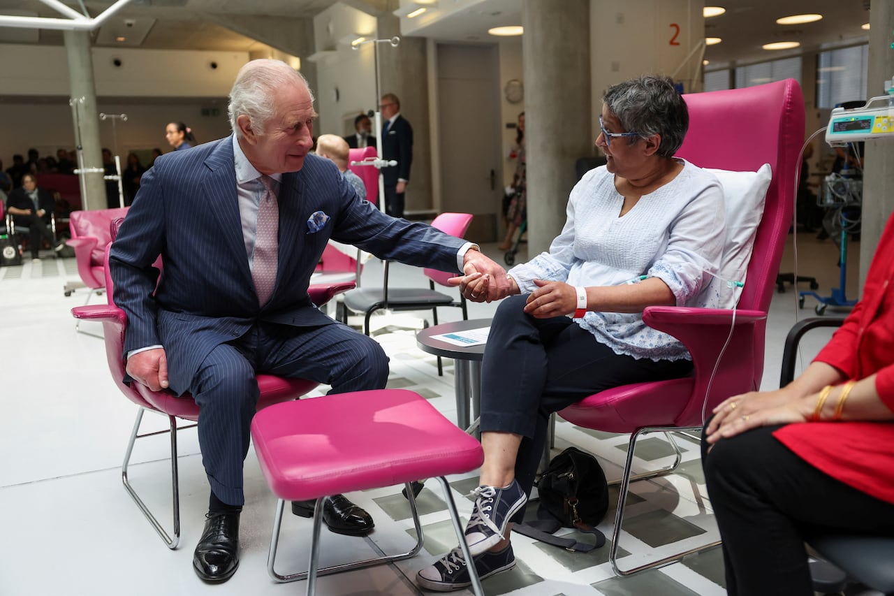 A person holds the hand of another person as the both sit in chairs.