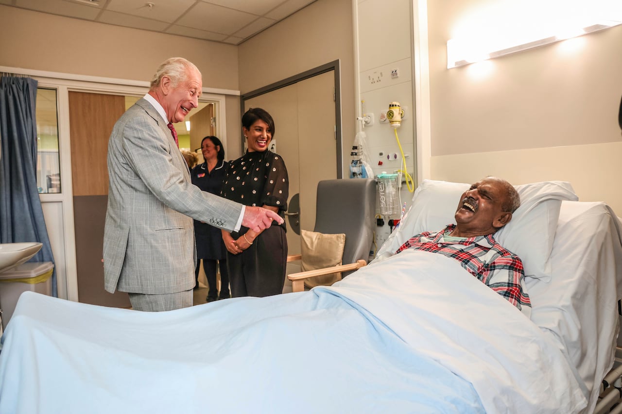 A person standing talks to another person lying in a hospital bed.
