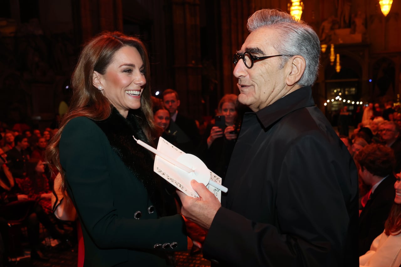 Two people smile as they talk to one another. One is holding a white candle and an order of service.