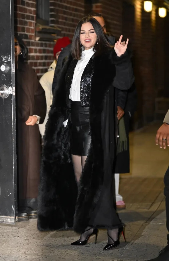 Selena Gomez wearing a long black coat with faux-fur trim over a mini skirt