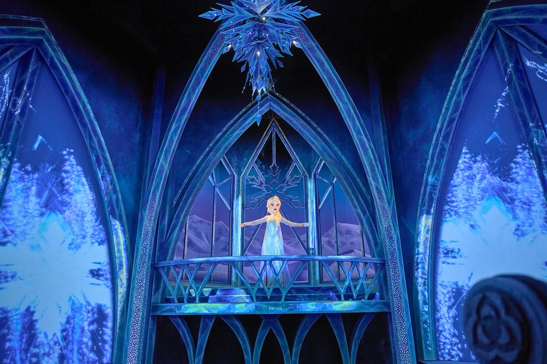 An animated woman in a blue dress stands on an icy balcony, snowflakes glowing like at Frozen Ever After—your 9/9/25 Disney recap.