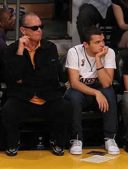 Five people sit courtside at a basketball game, all wearing casual attire. Some wear Lakers-themed clothing
