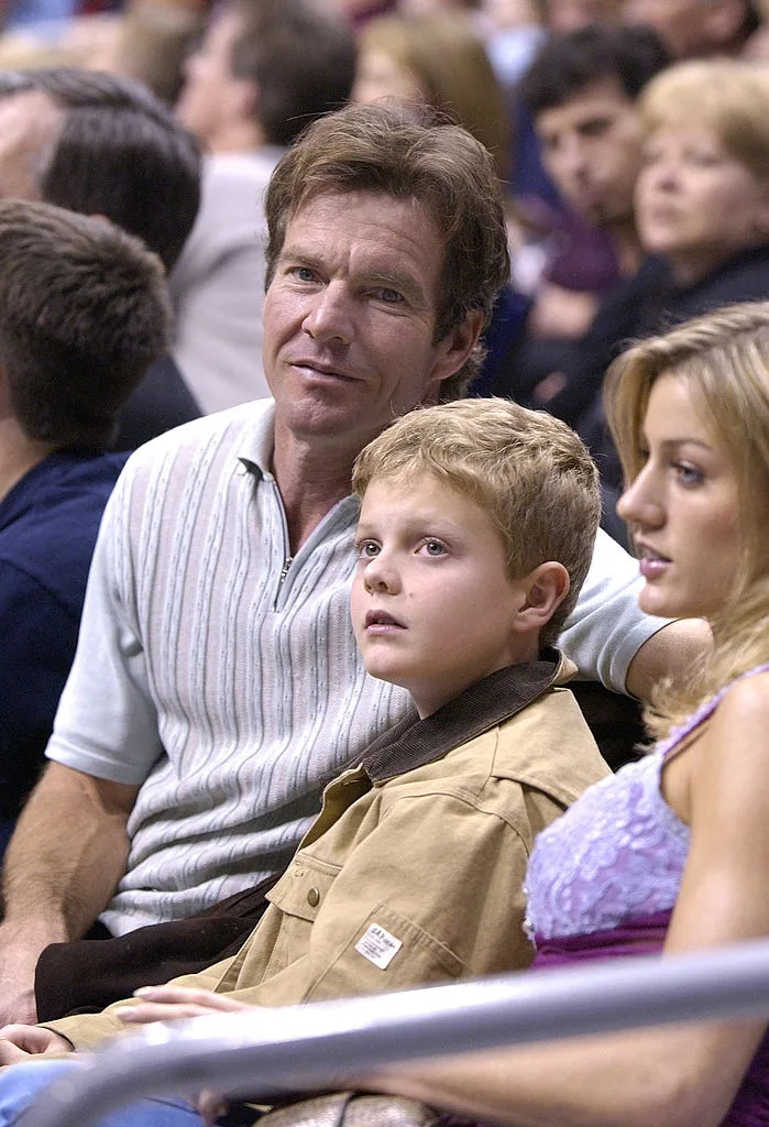 Man, boy, and woman sitting in audience at an event, looking ahead with curious expressions. The man wears a striped shirt; the boy, a jacket