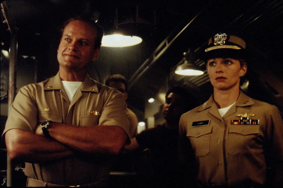Two actors in a scene wearing naval uniforms, appearing serious on a ship set. The setting suggests a military or dramatic narrative