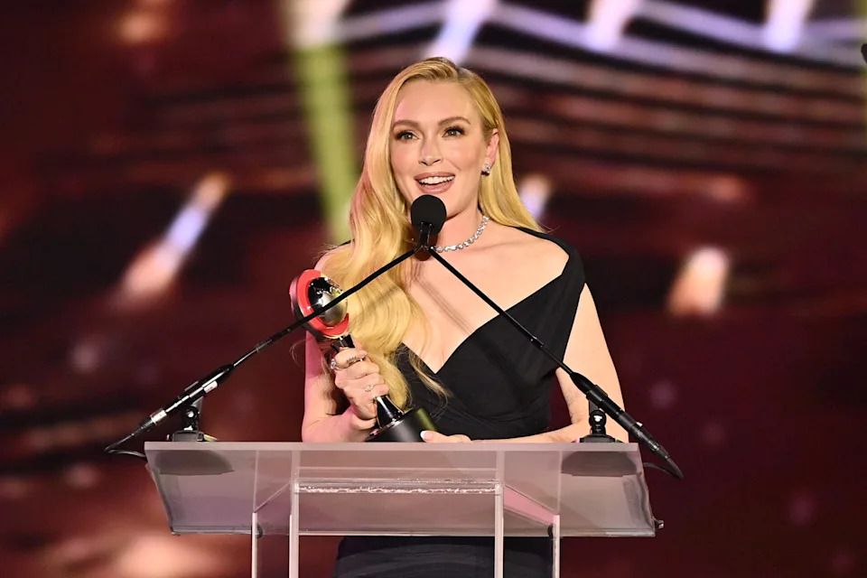 Lindsay Lohan in a stylish dress holds an award while speaking at a podium on stage