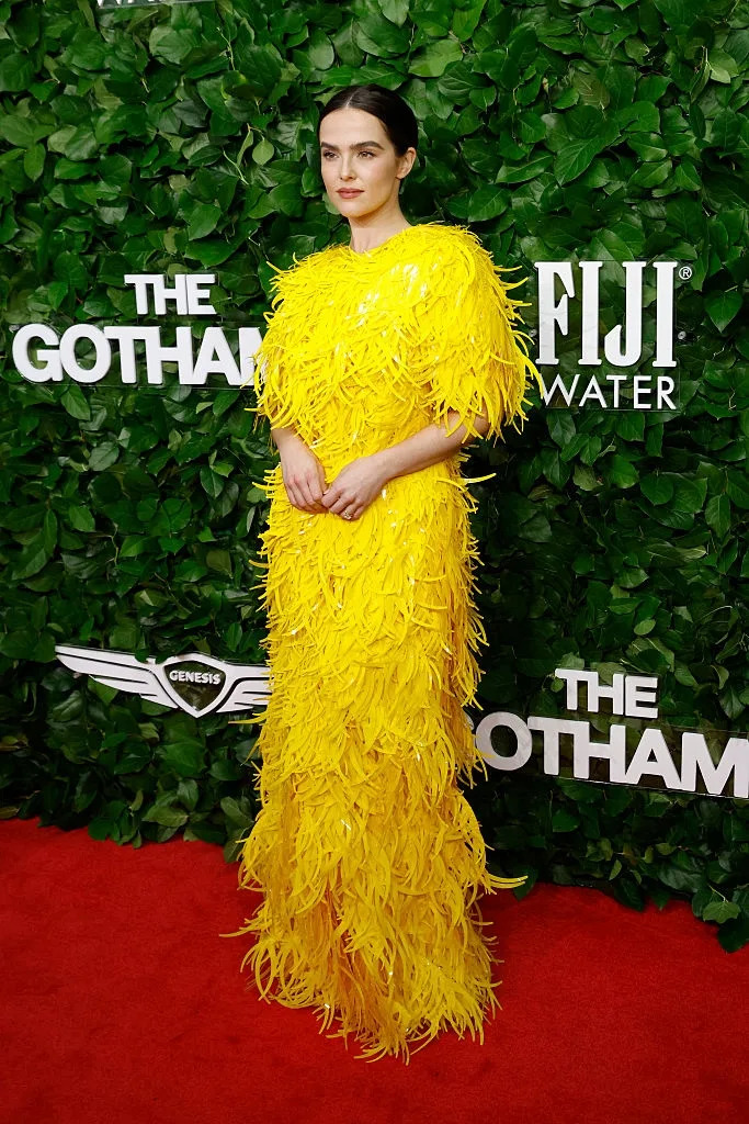 Person on red carpet in a striking feathered gown standing in front of a leafy backdrop