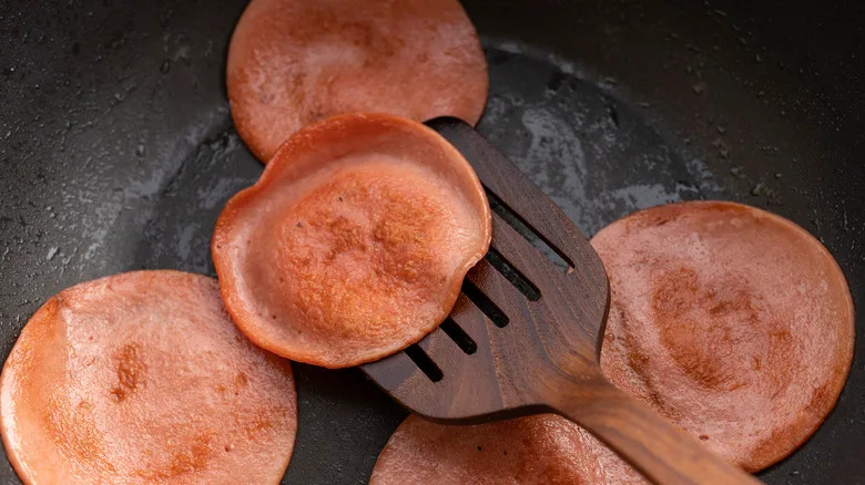 Fried bologna on a pan with a wooden spatula