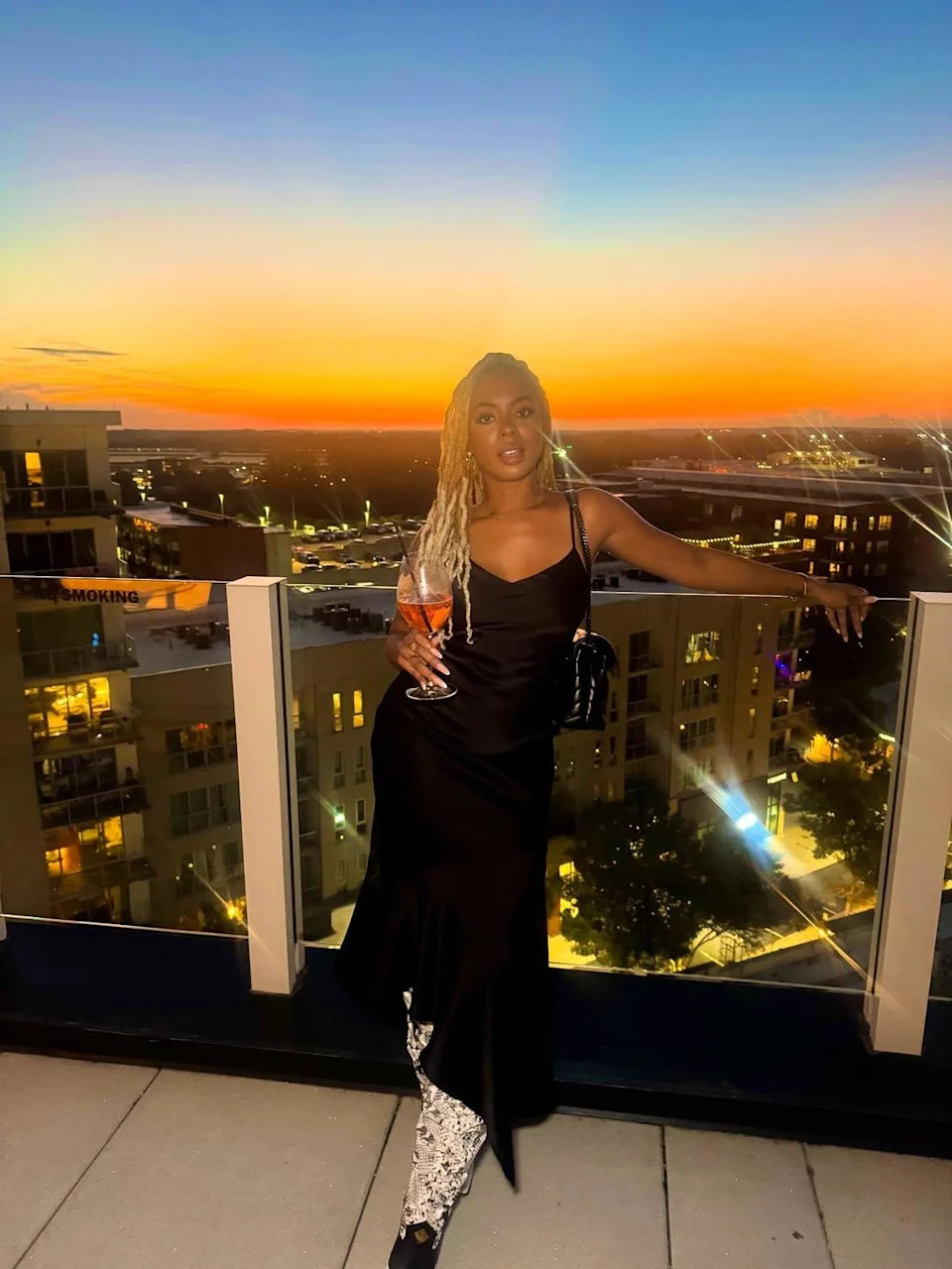 Mickey Lee posing in front of a sunset on a rooftop bar