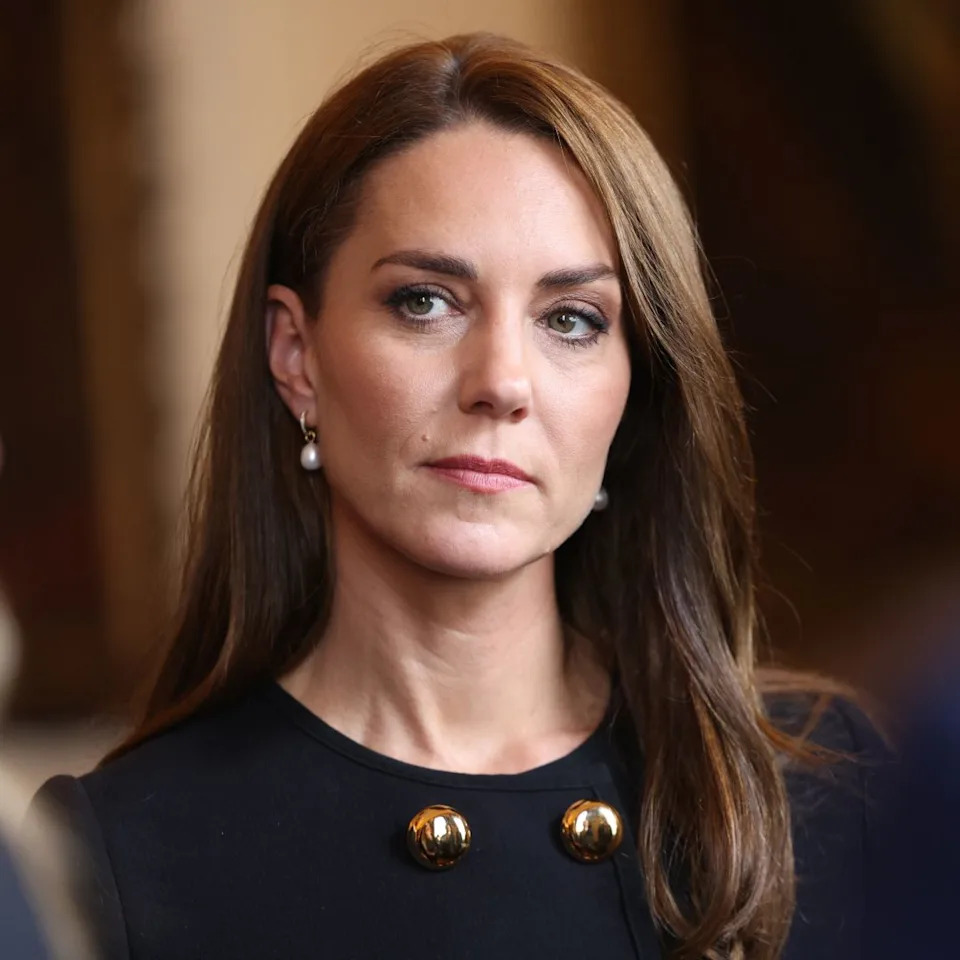  Kate Middleton has long brunette hair and wears a black outfit. 