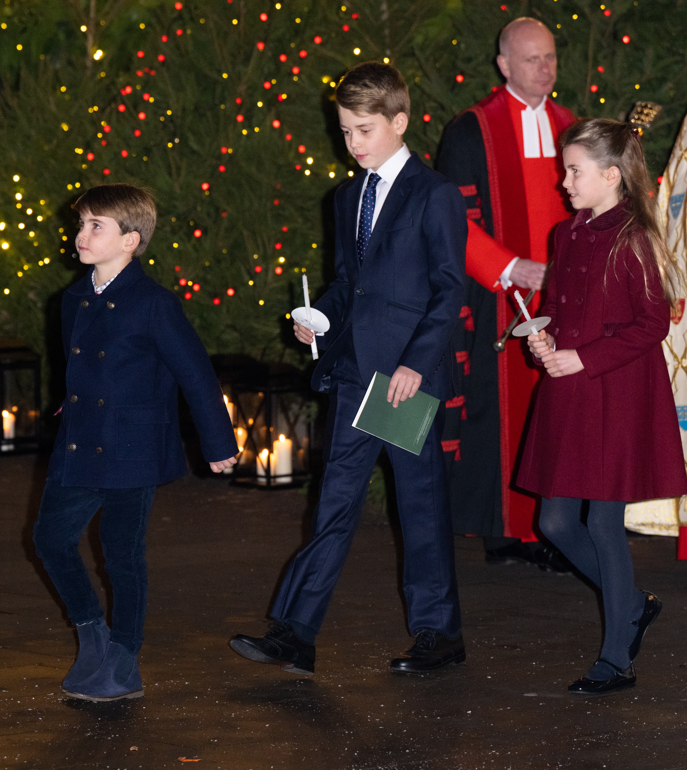Prince George, Prince Louis and Princess Charlotte holding Christmas candles walking in front of a tree