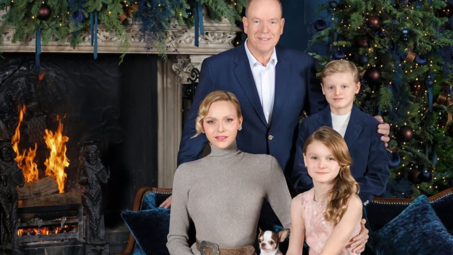 Monaco’s Royal Family Ditches Christmas Sweaters for Luxury Princess Charlene wears a long taupe dress with a pleated skirt, long sleeves, and a turtle neck, and poses next to a burning fireplace and a Christmas tree with her pet dog, her twin children, Princess Gabriella and Prince Jacques, and husband Prince Albert