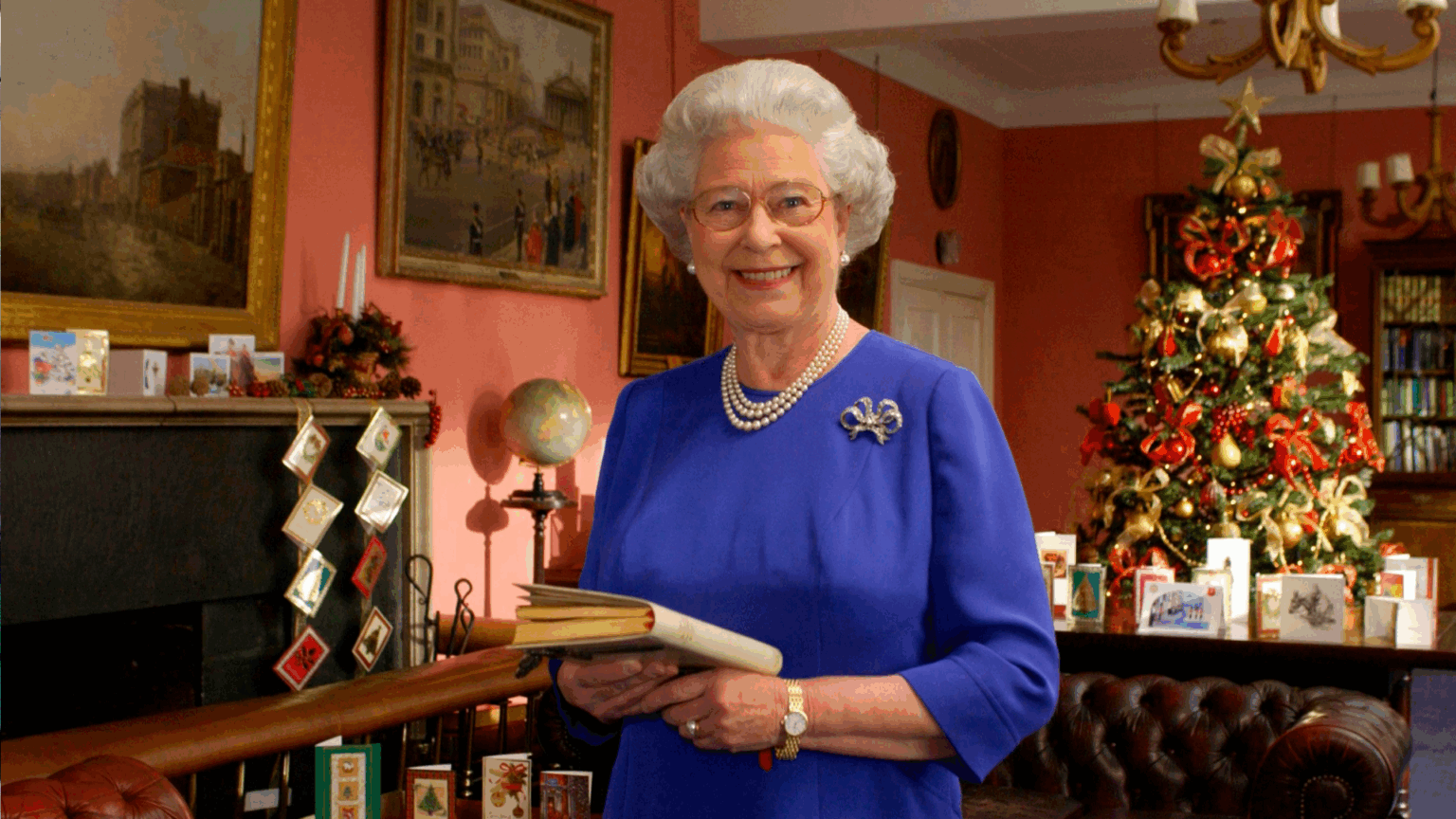Former Royal Butler Reveals the “Hilarious” Christmas Fire Fiasco that Made the Royal Family “Collapse With Laughter” Queen Elizabeth wearing a blue dress standing in front of a Christmas tree