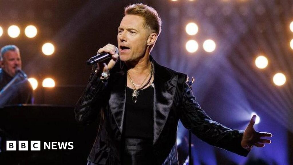 Ronan Keating on his New Year’s Eve show and reuniting Boyzone in 2026 Ronan Keating performing on stage at the Riverside Studios, holding a microphone and wearing a black vest and black leather jacket