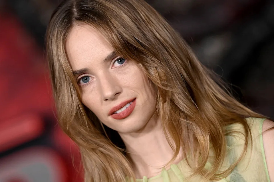 Maya Hawke with long hair poses confidently at an event, wearing a stylish outfit with soft makeup