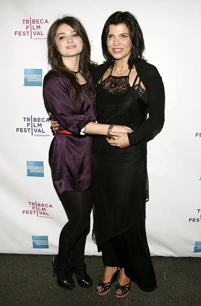 Two women smiling, standing together at an event. One in a purple dress, the other in a black lace dress and heels. Tribeca Film Festival backdrop