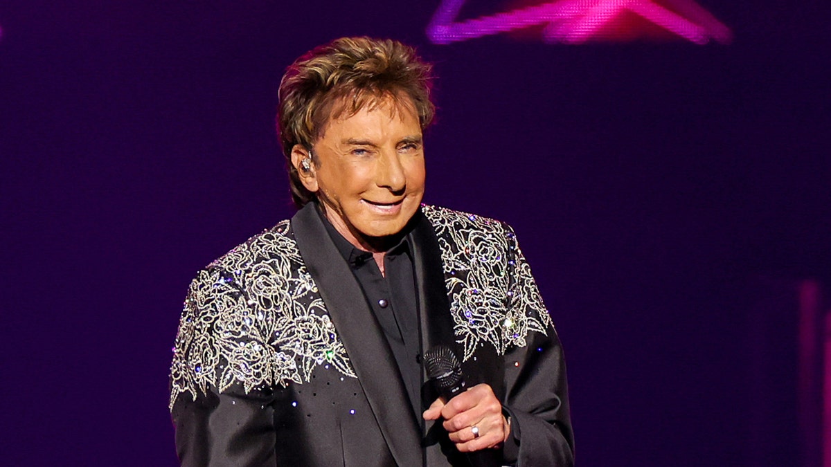 Barry Manilow holds a microphone on stage