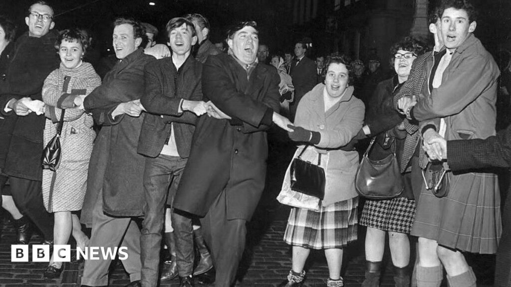 Why did Edinburgh become the home of Hogmanay? A black and white photo of people singing Auld Lang's Syne during New Year at the Tron, Edinburgh 1964.
