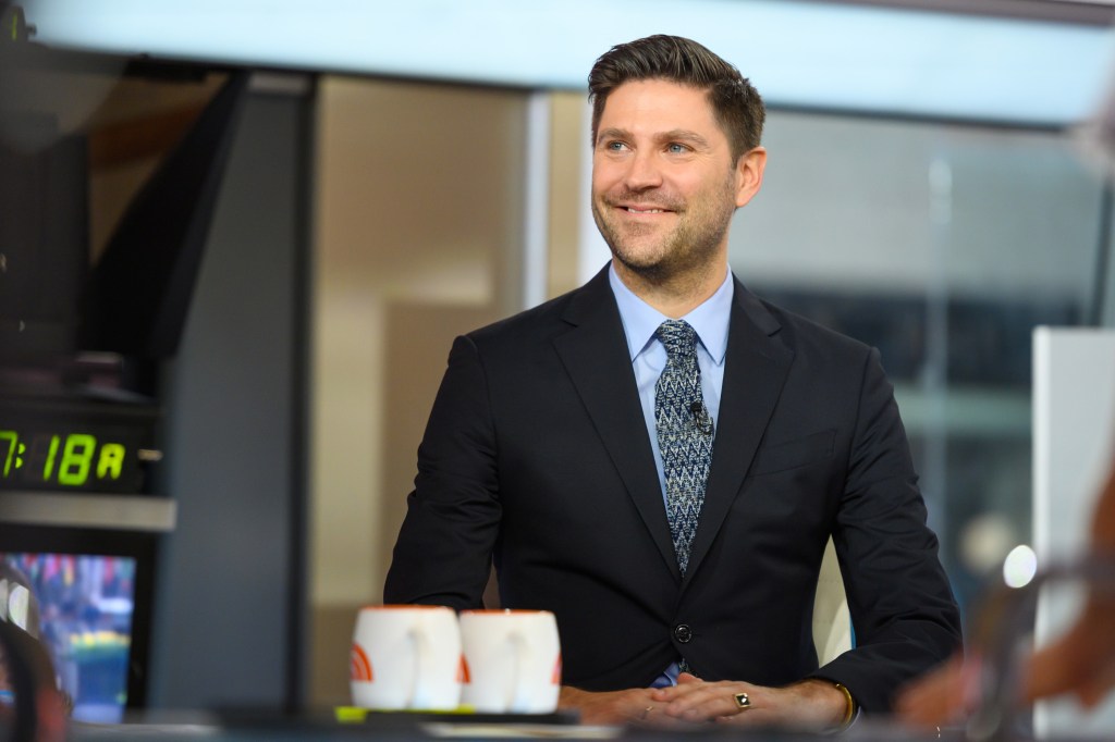 Dan Wakeford smiling in a black suit and patterned tie.