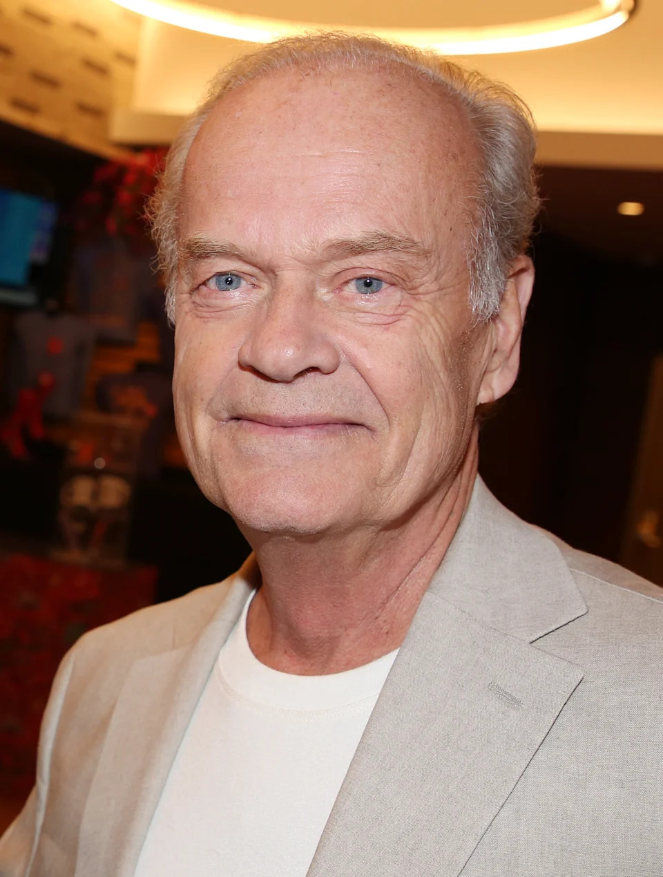 Person in a casual white shirt and light blazer at an event, standing indoors with a subtle smile