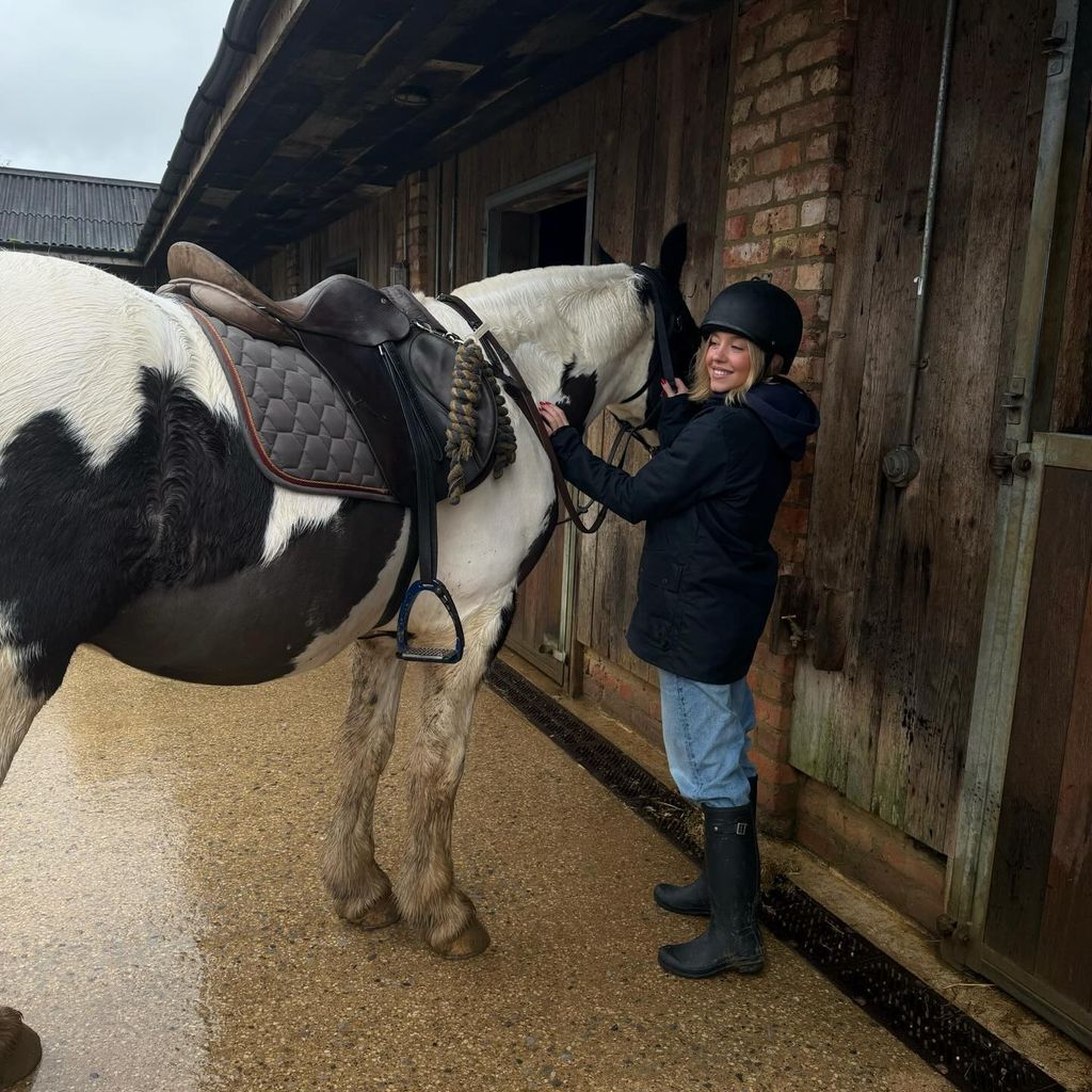 Sydney Sweeney wears equestrian gear and pats a big black and white horse in a stable