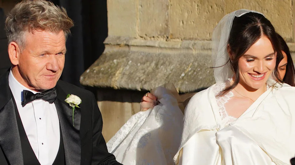 Gordon Ramsay pictured entering Bath Abbey with his daughter Holly. He is wearing a black suit and she is wearing a white dress and veil.