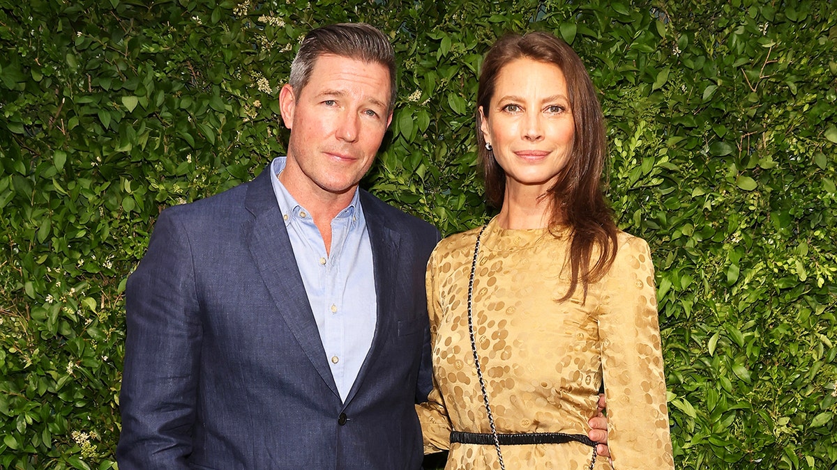 Ed Burns and Christy Turlington standing side-by-side smiling against a grassy backgroup.