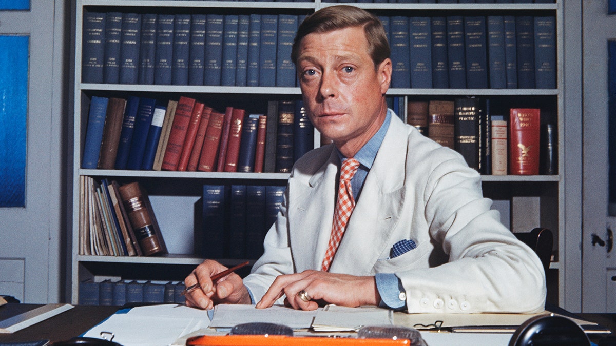 Edward VIII, sitting at his desk wearing a beige suit.