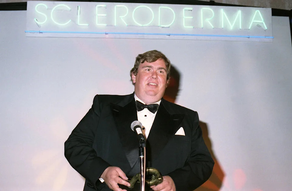 Man in a tuxedo speaks at a microphone during a Scleroderma event
