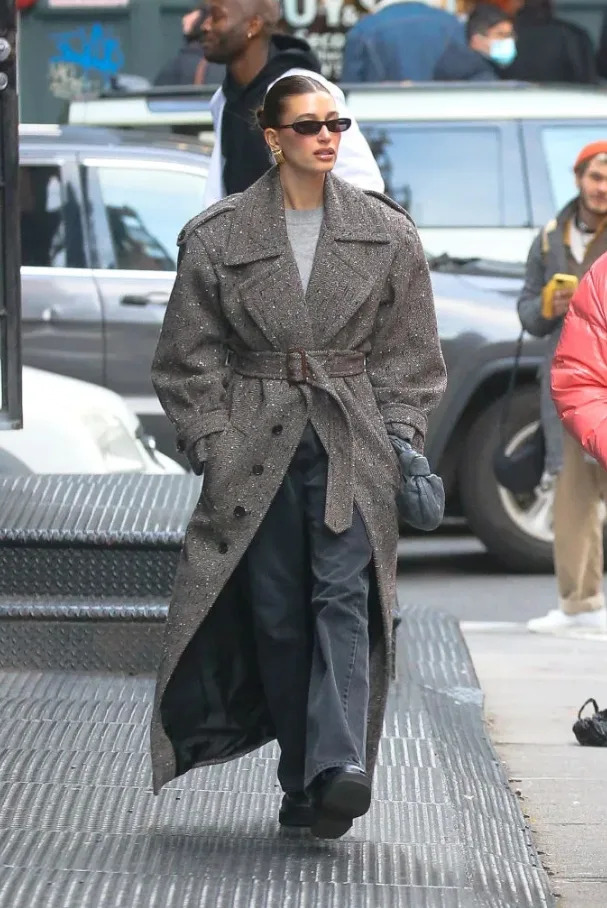 Hailey Bieber in an oversized belted gray coat with wide-leg pants and sunglasses