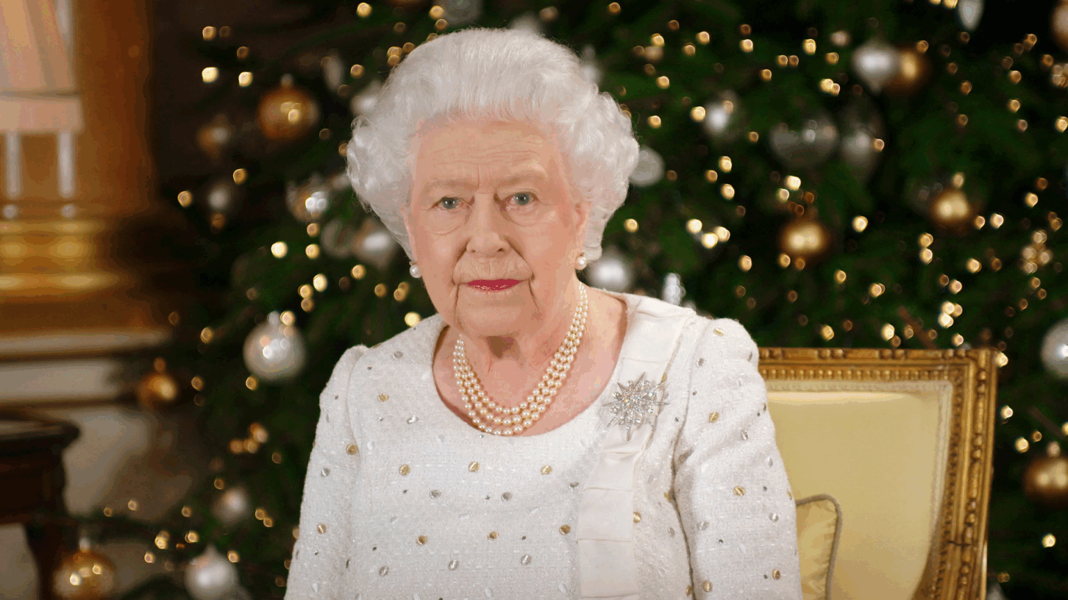 Queen Elizabeth “Banned” This “Vicious” Game During Sandringham Christmas Celebrations Queen Elizabeth wearing a white dress sitting in front of a Christmas tree