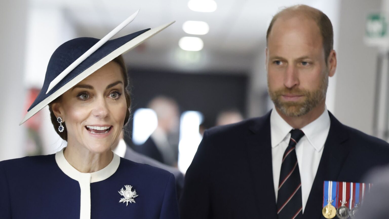 Expert Claims Kate Middleton Is Aware of Fury Over New Home Kate Middleton wears a navy dress with white accents and a matching hat while Prince William wears a suit with medals