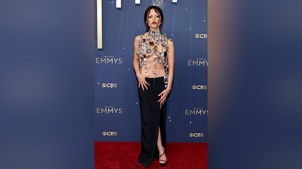 Jenna Ortega poses on the red carpet wearing a jewel-encrusted top and black skirt with a thigh-high slit.