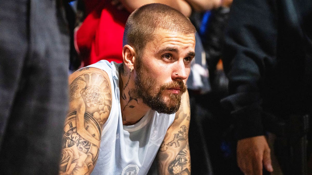 A close-up of Justin Bieber wearing a sleeveless white shirt looking reflective.