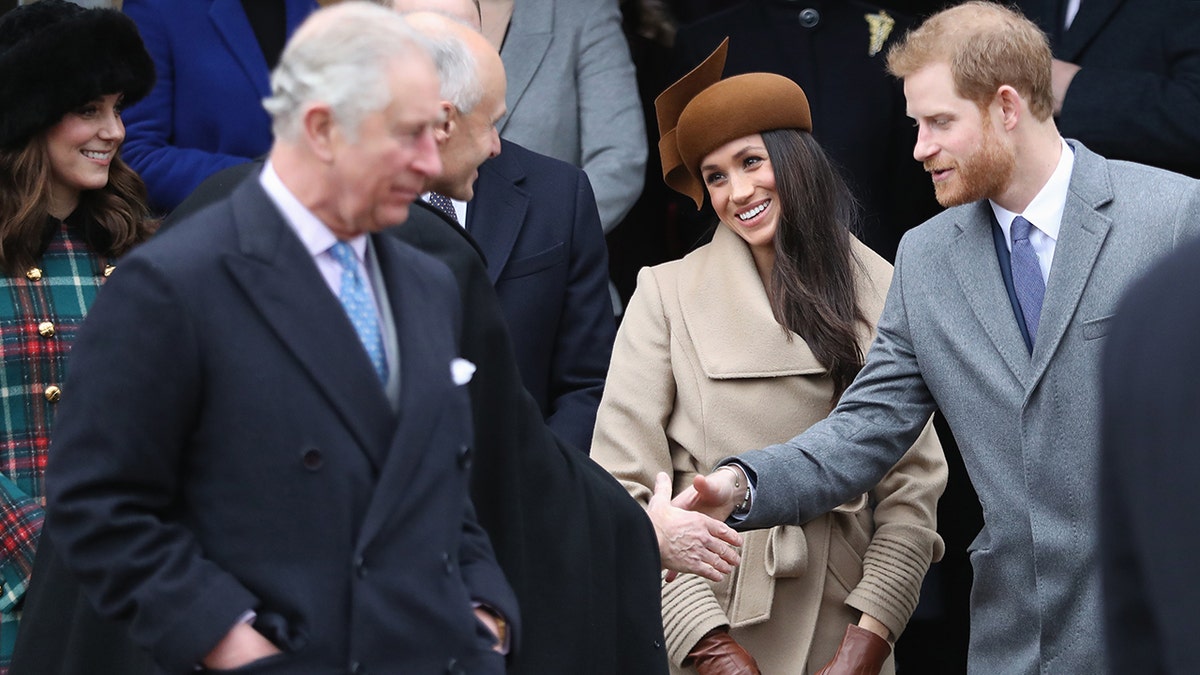 Prince Harry and Meghan Markle greeting a guest as King Charles walks on.