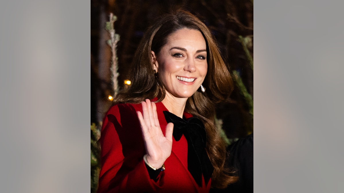 A close-up of Kate Middleton waving in a red coat dress.