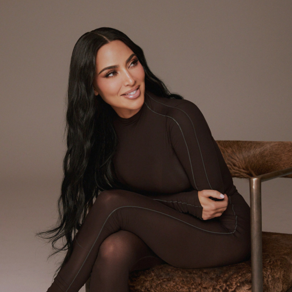 Kim Kardashian wearing a dark brown bodysuit, sitting on a furry brown chair.