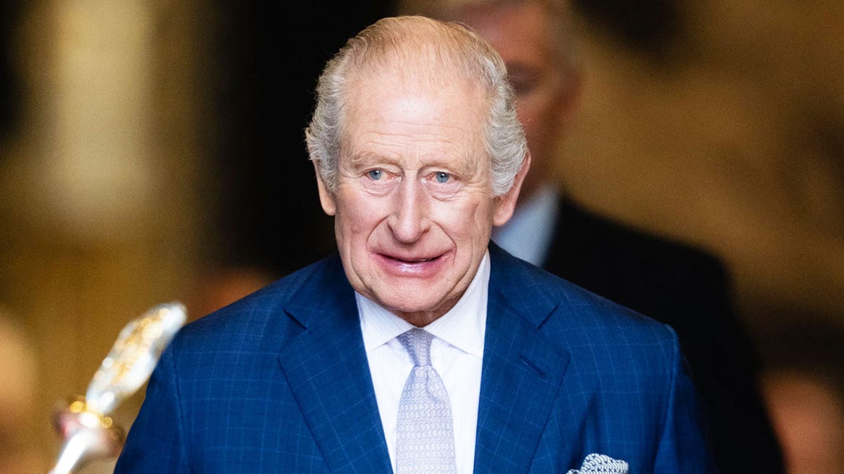 A close-up of King Charles smiling in a blue suit.