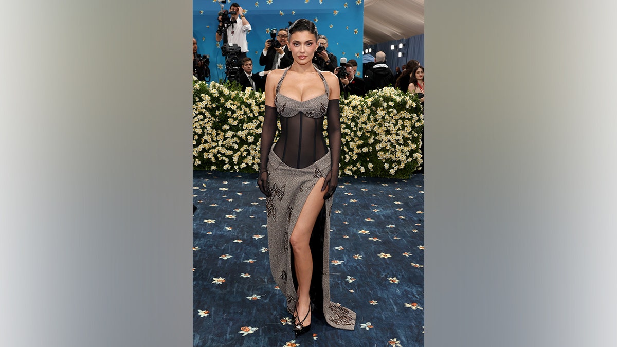 Kylie Jenner poses on the Met Gala carpet wearing a sheer corset gown with a plunging neckline and high slit.