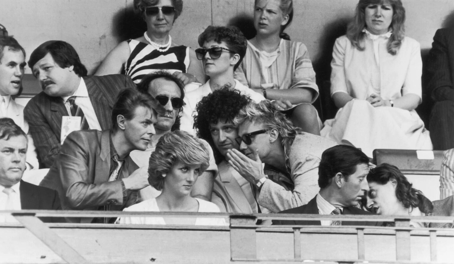 David Bowie chats with Roger Taylor and Brian May of Queen, sitting behind Princess Diana during the Live Aid Concert at Wembley Stadium (13th July 1985)