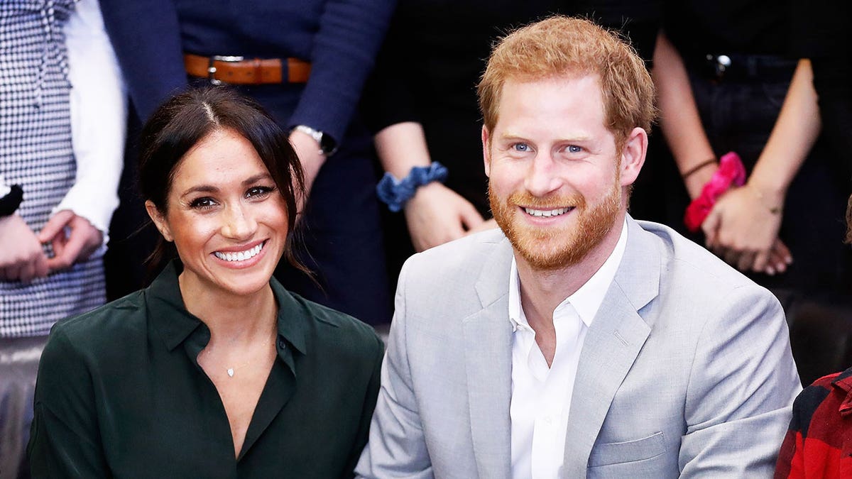 Meghan Markle and Prince Harry sitting next to each other and smiling.
