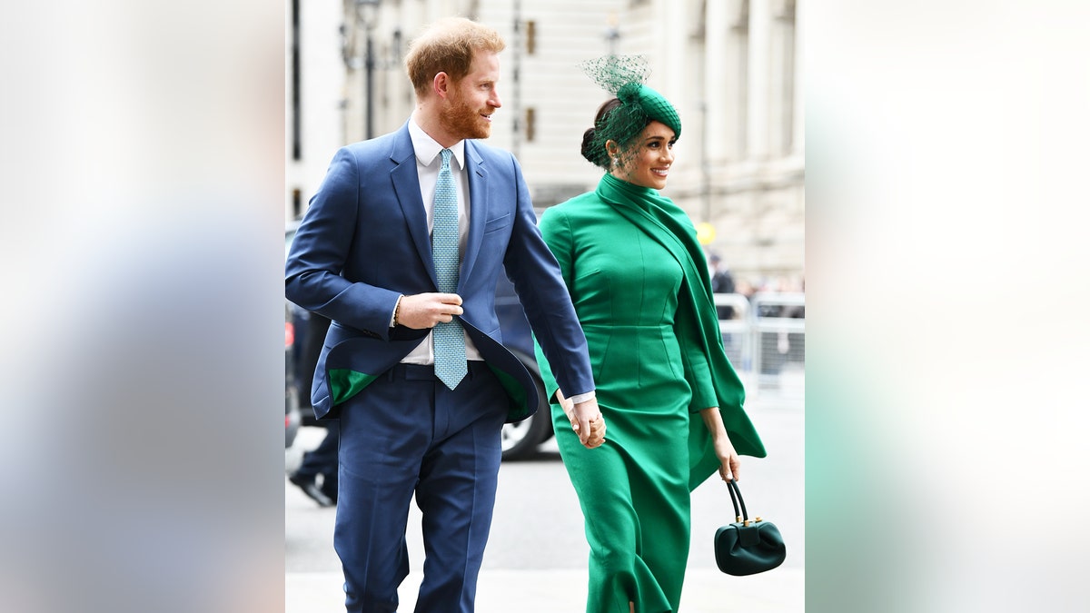 Prince Harry wearing a blue suit and Meghan Markle wearing a green dress as they walk together outdoors.