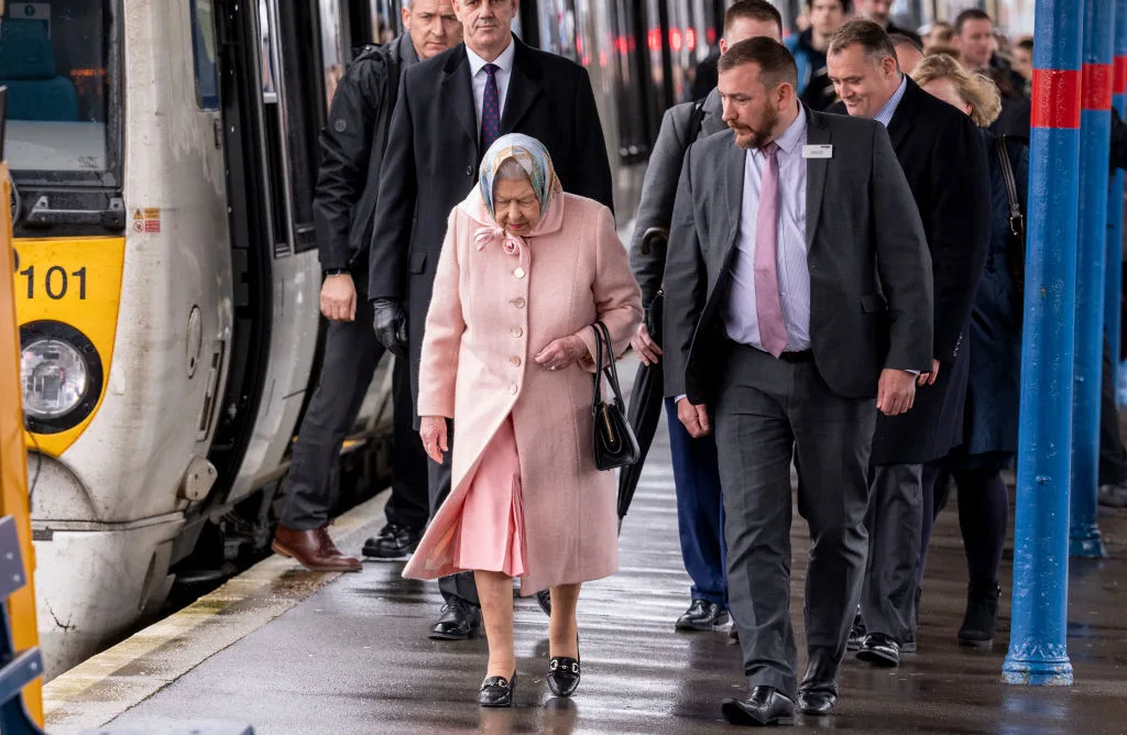 The Queen accommpanied by guards walking away from train