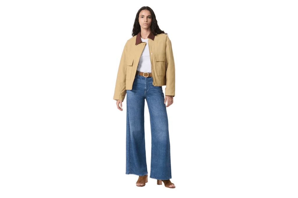 A woman wearing a tan jacket, white t-shirt, wide-leg jeans, and brown sandals.