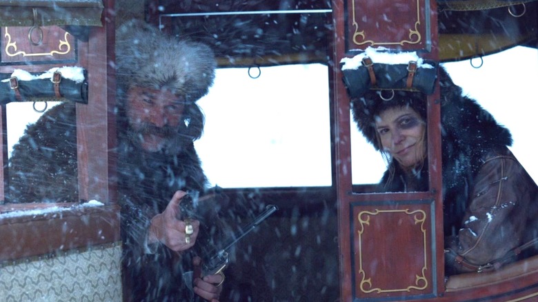 Kurt Russell as John Ruth holding a gun and sitting in a carriage with Jennifer Jaosn Leigh as Daisy in The Hateful Eight