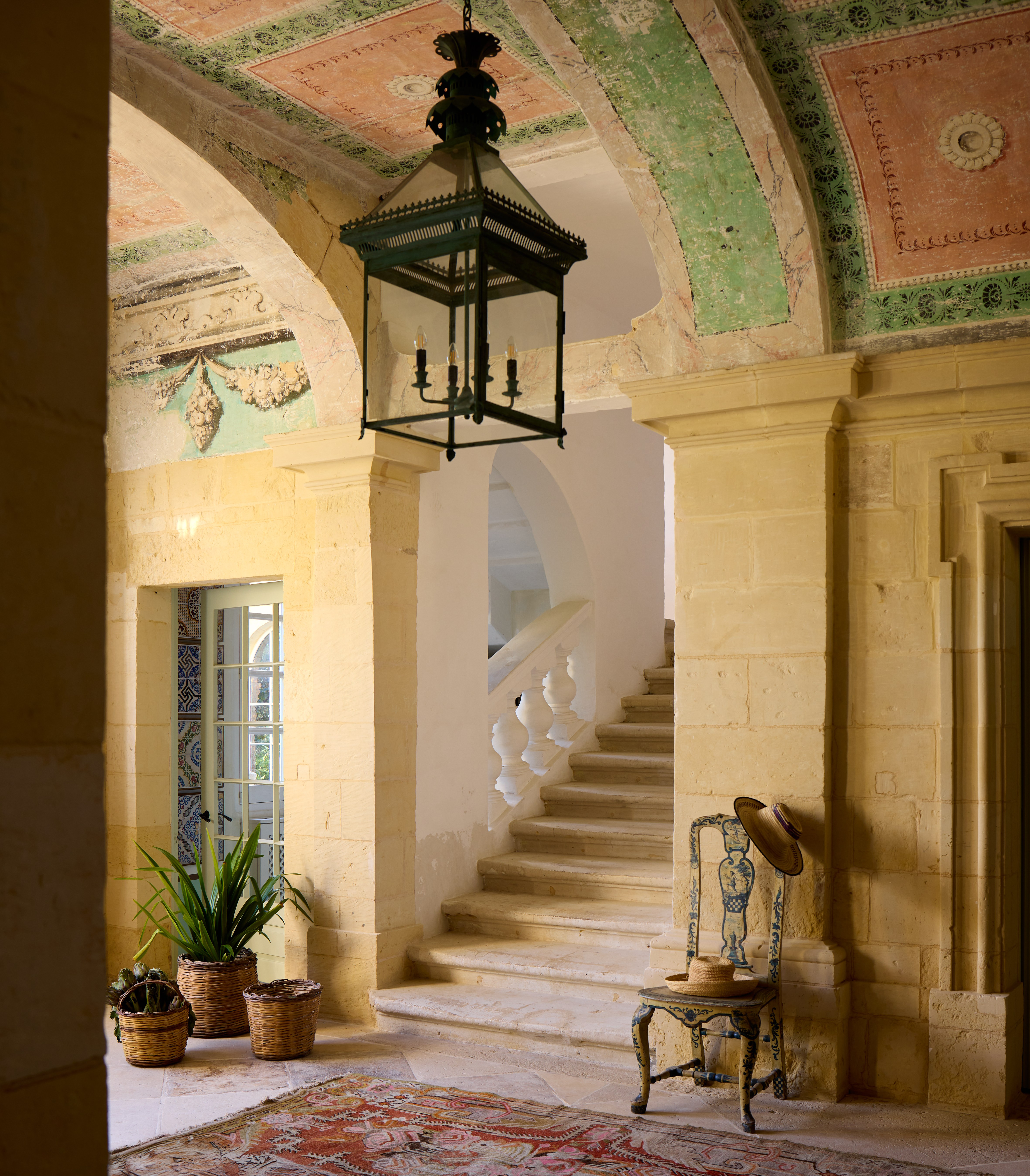 A hallway in Casa Bonavita, Malta, with a mosaic floor, painted archways, and a staircase.