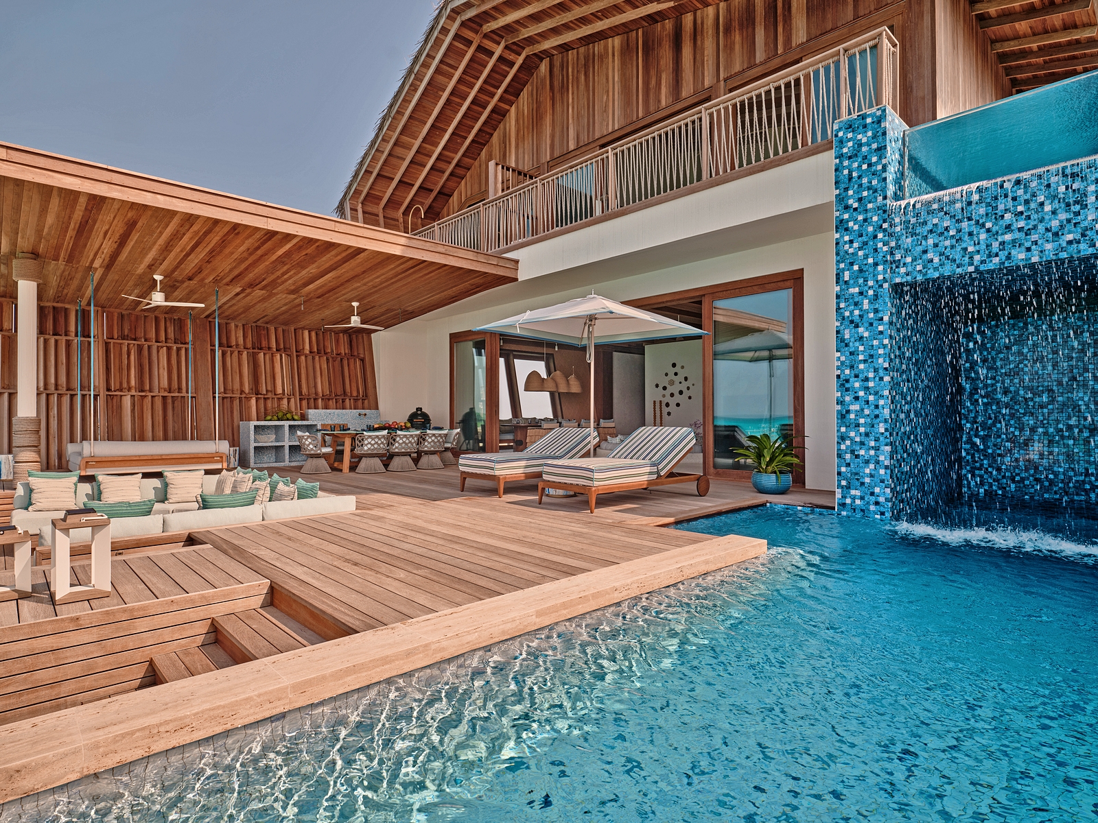 A luxury resort in the Maldives with a private deck, pool, and waterfall feature.